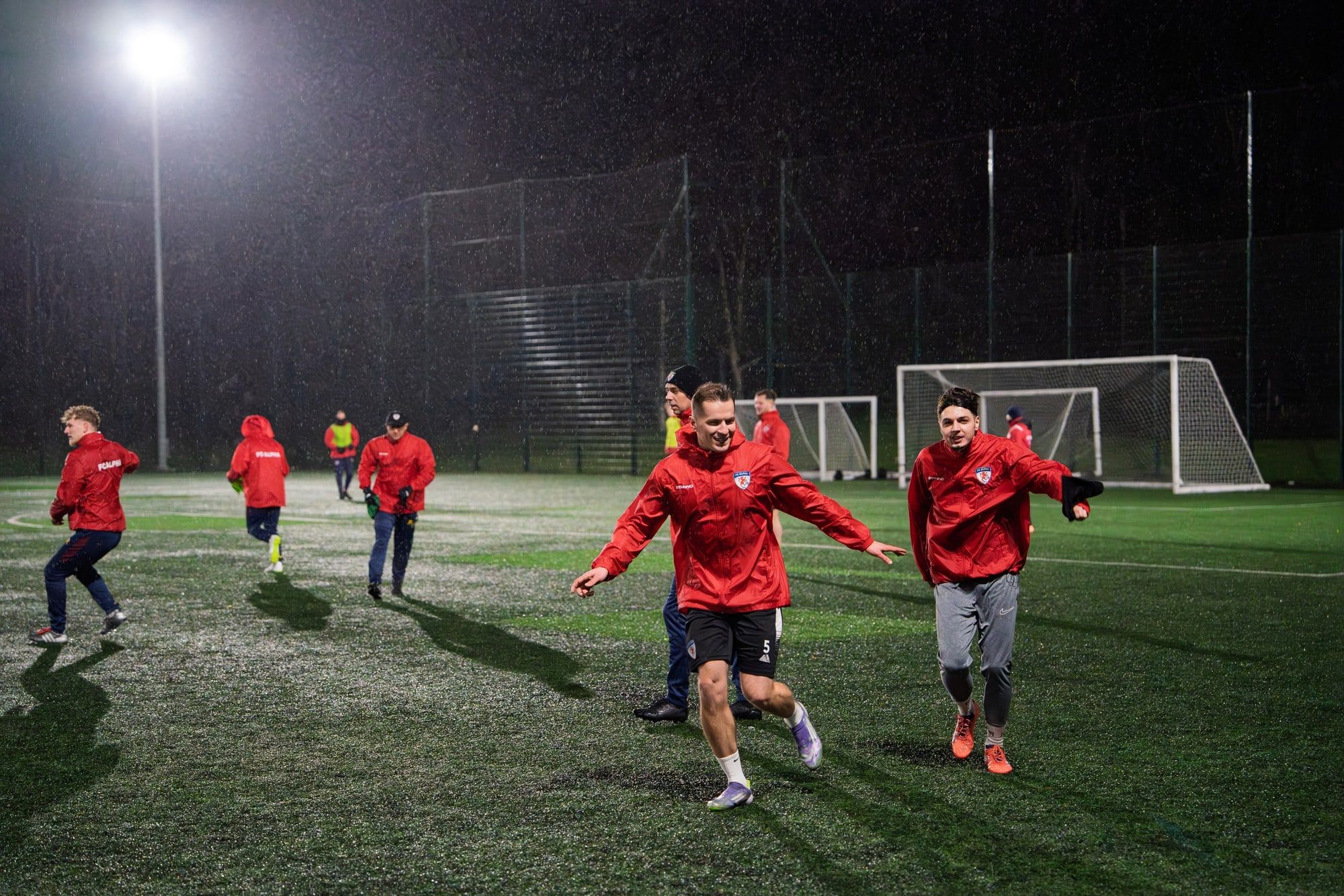 Senior players chasing the ball in a small-sided game under floodlights