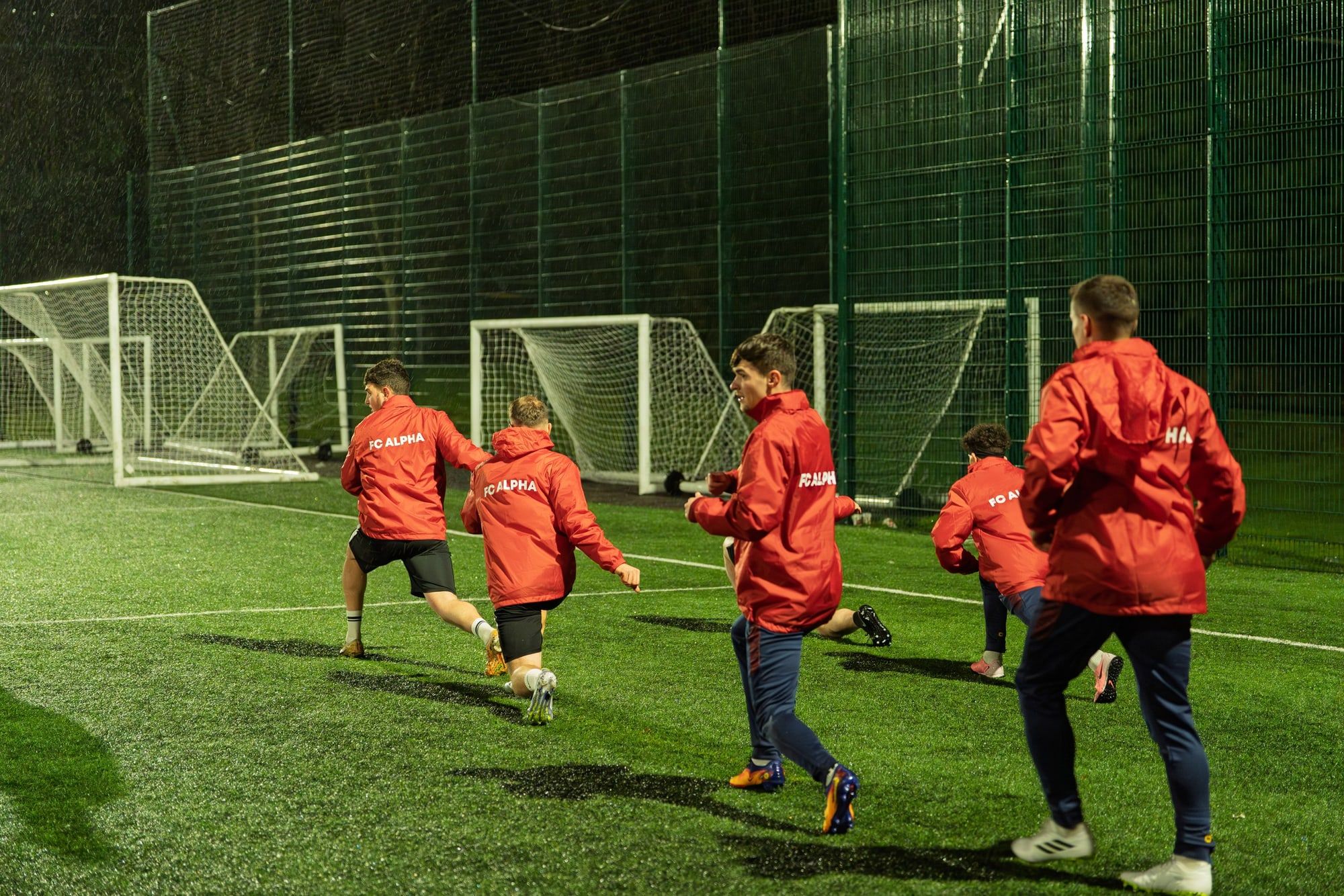 Senior players running a drill on a floodlit pitch